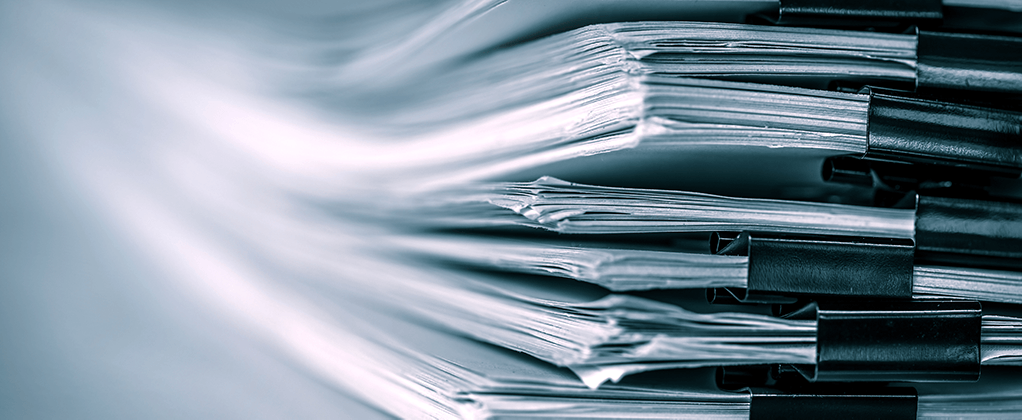 Close up photo of a pile of reports held together with bulldog clips