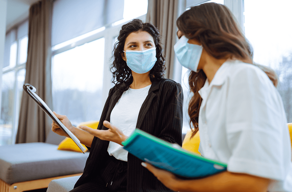 Two woman wearing masks and working together