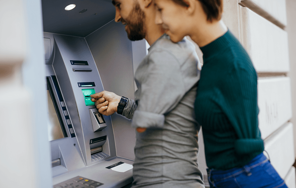 Photo of a couple who are each missing an arm, using an ATM