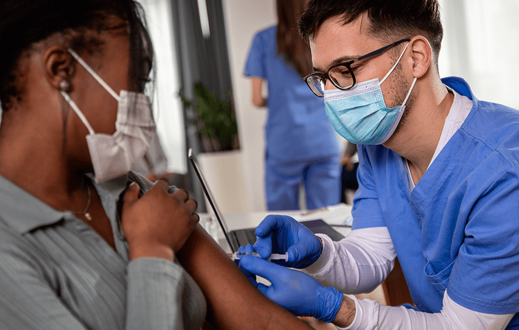 Photo of a male nurse giving the COVID-19 vaccine to a woman.