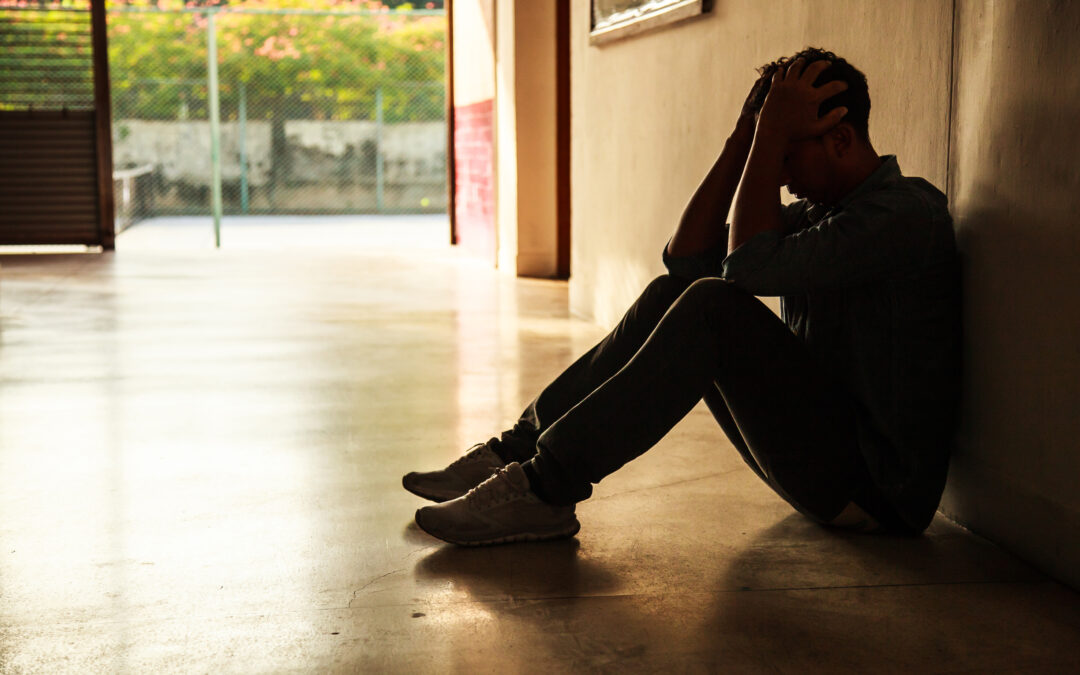Man sitting holding head in hands, in a dark corner needing help.